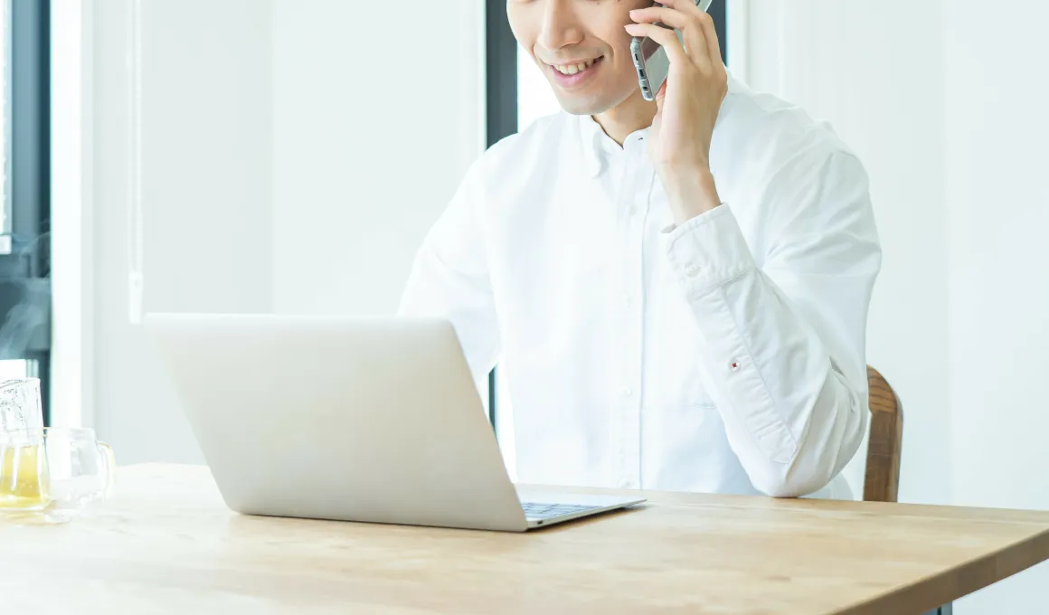 PCの前で電話する男性